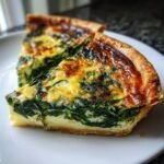 Two golden-brown slices of rich Spinach Quiche featuring a deep green spinach filling and a flaky crust, served on a white plate.