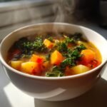 Close-up of a steaming white bowl filled with hearty Winter Vegetable Soup, featuring chunks of orange squash and green kale.