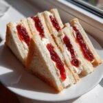Four triangular halves of Strawberry Jam Cheese Wedges Tea Sandwiches stacked on a white plate.