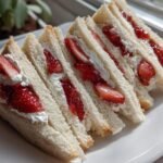 Close-up of several triangular Strawberry Jam Cheese Wedges Tea Sandwiches filled with cream and fresh strawberries.