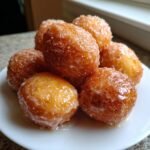 A stack of golden-brown, freshly fried Vegan Glazed Donut Holes glistening with a thin sugar glaze.