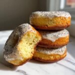 Stack of three Vegan Lemon Poppy Seed Donuts with one donut broken open showing the moist interior.