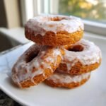 A stack of four golden brown Baked Vegan Pumpkin Spice Donuts covered in a thick white glaze.