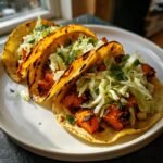 Three delicious BBQ Butternut Squash Tacos filled with charred squash and cabbage slaw, served on a white plate.