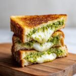 A stack of two halves of a Broccoli Pesto Grilled Cheese sandwich showing gooey, melted cheese and vibrant green pesto.