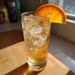 A tall glass filled with ice and a sparkling Citrus And Honey Mocktail, garnished with an orange slice.