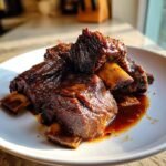 A close-up of tender, glazed Cozy Slow Cooker Short Ribs stacked on a white plate with rich sauce.