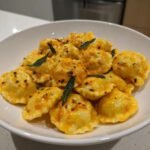 Close-up of Cozy Sun Dried Tomato Pumpkin Ravioli tossed in a creamy sauce and garnished with fried sage leaves.