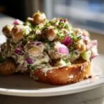 Close-up of a creamy Delightful Chickpea Salad piled high on toasted bread, featuring chickpeas, red onion, and herbs.