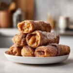 A stack of golden brown Crispy Apple Pie Rolls coated in cinnamon sugar, with two cut open showing the apple filling.