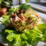 A scoop of Delicious Salmon Salad Recipe Fresh Flavorful Delight mixed with celery, served atop a crisp lettuce leaf and garnished with dill.