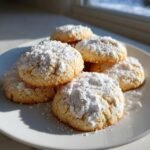 A stack of Delightful Italian Christmas Cookies generously dusted with white powdered sugar on a white plate.