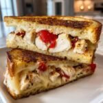 Close-up of an Everything Chicken Tomato Grilled Cheese sandwich, cut in half, showing melted cheese, chicken pieces, and tomato filling.