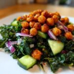 A vibrant serving of Healthy Loaded Kale Salad topped generously with spicy chickpeas, red onion, and cucumber slices.