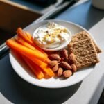A plate showing healthy snacking options: carrot sticks, almonds, whole grain crackers, and a small bowl of creamy dip.