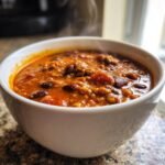 Close-up of a steaming white bowl filled with rich, thick Hearty Pumpkin Chili Recipe, featuring ground meat and kidney beans.