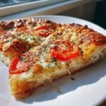 A close-up view of two slices of Herbed Butter Tomato Pizza showing a thick, fluffy crust, melted cheese, and fresh tomato slices.