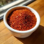 Close-up of vibrant red Homemade Cajun Seasoning blend filling a small white bowl on a wooden surface.