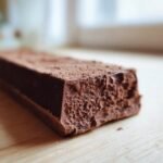 Close-up of a rich, dark Homemade Vegan Oat Milk Chocolate Bar showing its textured, slightly crumbly interior dusted with cocoa powder.