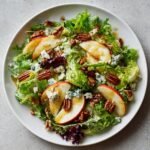 Overhead view of a Delightful Autumn Harvest Honeycrisp Apple Salad with pecans, blue cheese crumbles, and vinaigrette.