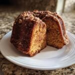 A slice cut from an Irresistible Apple Cider Cake, topped with cinnamon sugar and chopped pecans.