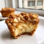 Close-up of an Irresistible Apple Crisp Mini Cheesecakes with a bite taken out, showing creamy filling and apple topping.