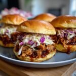 Close-up of Irresistible BBQ Chicken Sliders piled high with saucy chicken and colorful coleslaw on soft buns.
