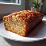 A golden-brown loaf of Irresistible Cake Mix Banana Bread resting on a white plate.