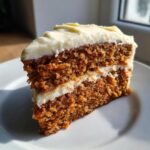 A perfectly layered slice of Irresistible Carrot Cake Recipe topped with thick cream cheese frosting, sitting on a white plate.