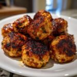 A close-up of several perfectly browned and glazed Irresistible Chicken Harissa Meatballs piled on a white plate.