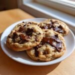 Four warm, thick Irresistible Chocolate Chip Cookies piled on a white plate with melted chocolate pools.