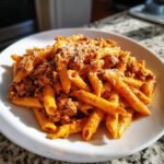 A close-up of a white plate piled high with Irresistible Creamy Beef Pasta, topped with grated cheese.