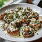 A white plate filled with Irresistible Creamy Garlic Parmesan Mushrooms, topped with melted cheese and fresh parsley.