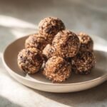 A stack of homemade Irresistible Energy Balls coated in sesame seeds and chocolate chunks on a light plate.