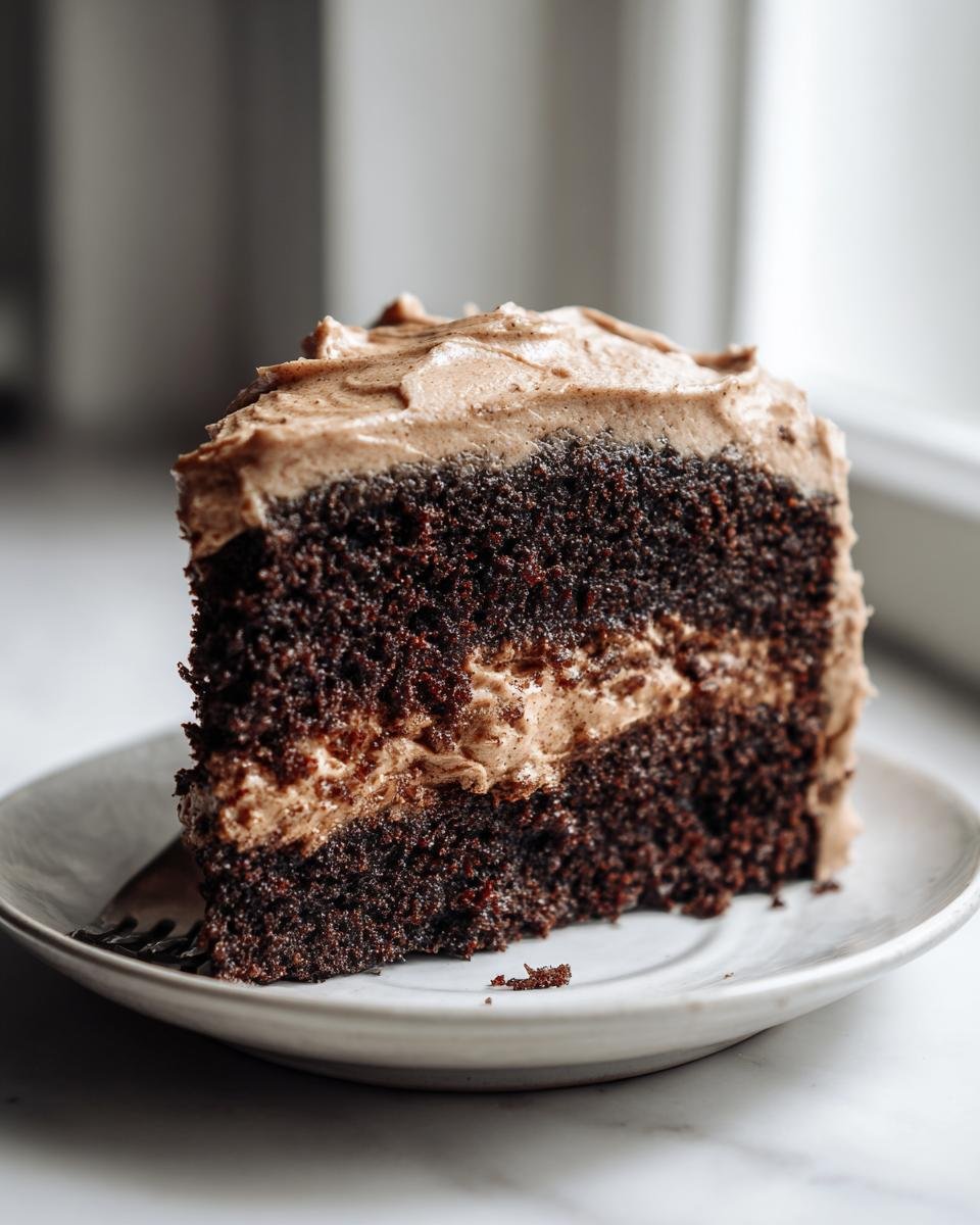 Close-up of a moist slice of dark chocolate cake layered with light brown frosting, part of an Irresistible Gingerbread Cake.
