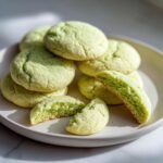 A stack of soft, pale green Irresistible Pistachio Cream Cookies, with one cookie broken in half showing the creamy interior.