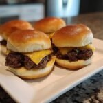 Close-up of two Irresistible Pumpkin Shaped Sliders Beef topped with melted cheddar cheese on a white platter.