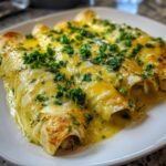 Close-up of three rolled tortillas covered in melted yellow queso sauce and fresh cilantro, featuring Irresistible Queso Chicken Enchiladas.