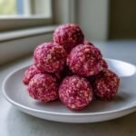 A stack of bright pink, textured Irresistible Raspberry Protein Balls made with oats, served on a white plate.