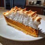 A tall slice of Irresistible Spiced Chai Pumpkin Meringue Pie showing the crust, pumpkin filling, and toasted meringue topping.