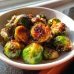Close-up of caramelized Brussels sprouts coated in a dark, glossy sweet sour sauce in a white bowl.