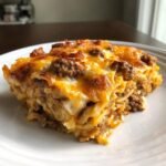 A close-up of a cheesy, layered slice of Irresistible Taco Casserole With Tortillas recipe on a white plate.