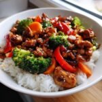 Close-up of Irresistible Teriyaki Chicken Stir Fry with broccoli, carrots, and peppers served over white rice in a bowl.