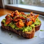 Close-up of Jerk Salmon Avocado Toast featuring seasoned salmon chunks over mashed avocado on dark toast.