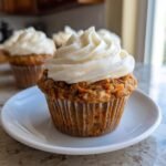 A close-up of one Irresistible Mothers Day Carrot Cake Muffin topped with thick cream cheese frosting on a white plate.