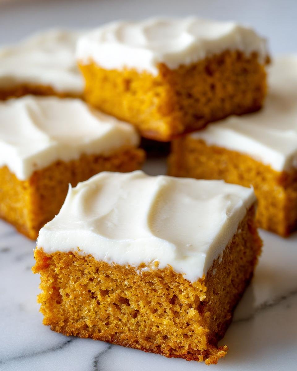 Close-up of several squares of Irresistible Old Fashioned Pumpkin Bars topped with thick cream cheese frosting.