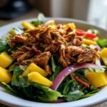 Close-up of Oven Baked Jamaican Jerk Chicken Salad featuring shredded jerk chicken, mango chunks, and red onion over greens.