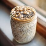 Close-up of Peanut Butter Chia Seed Overnight Oats topped with peanut butter, chia seeds, and oats in a glass jar.