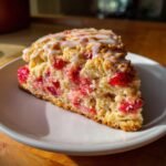 Close-up of a slice of Perfect Strawberry Oatmeal Scones, studded with bright red strawberries and topped with white icing.