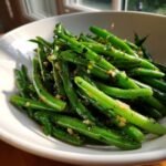 A white bowl filled with vibrant Sauteed Lemon Garlic Herb Green Beans, glistening with seasoning.